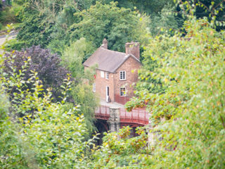 Lots of foliage in the foreground and in the middle distance a brick building and a glimpse of the Iron Bridge